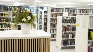 En vit blombukett på ett bord. I bakgrunden syns bibliotekets bokhyllor.